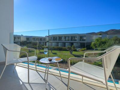 Balcone con due sedie e tavolino che si affaccia sul giardino e camere d'hotel moderne.