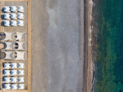 Vista aerea di una spiaggia di ciottoli con lettini, ombrelloni e acqua chiara verde-azzurra