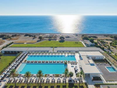 Großes Hotel mit mehreren Poolbereichen und Blick auf das Meer unter klarem Himmel.