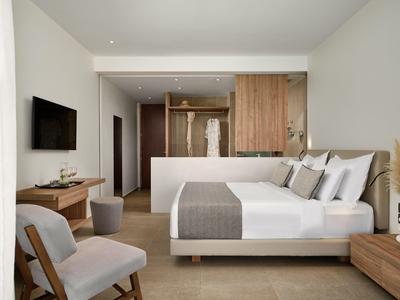 Camera d'hotel moderna con letto matrimoniale, TV, poltrona e angolo cottura in legno aperto.