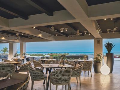 Offener Restaurantbereich mit Tischstühlen und Meeresblick bei Tageslicht.