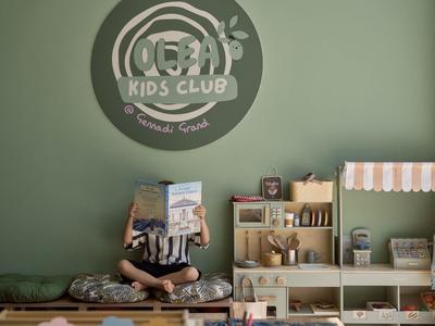 Gemütlicher Kinderclub mit Sitzkissen, Spielzeug und Lesenische in sanft grünem Raum.