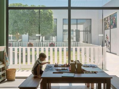 Hell beleuchteter Innenraum mit Holztisch und Kind, großer Glasfront mit Blick auf Garten und Terrasse.