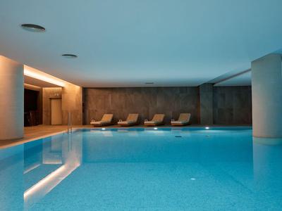 Moderner Innenpool mit hellem Wasser und Liegestühlen an der Wand.