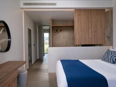 Modernes Hotelzimmer mit Doppelbett, blauem Läufer und offenem Holzkleiderschrank.