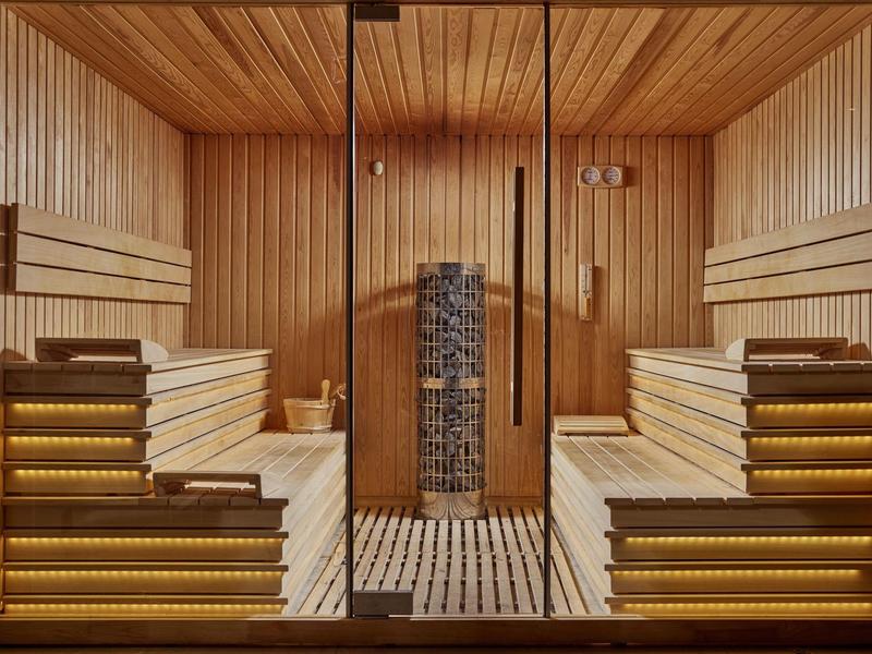 Sauna con rivestimento in legno, illuminazione calda e pietre al centro