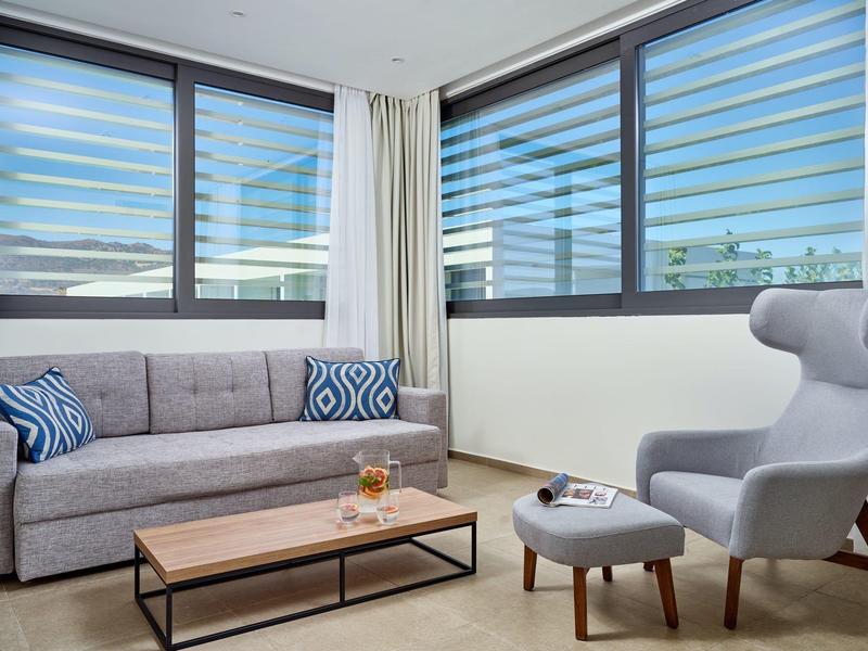 Soggiorno luminoso con divano grigio, poltrona e grande finestra con tende moderne.