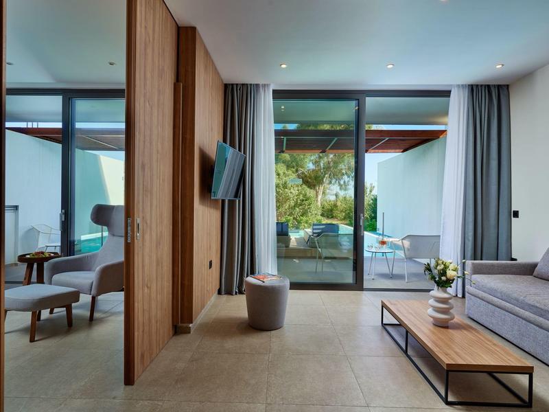 Camera d'hotel moderna con divano, poltrona e vista sulla terrazza con piscina.