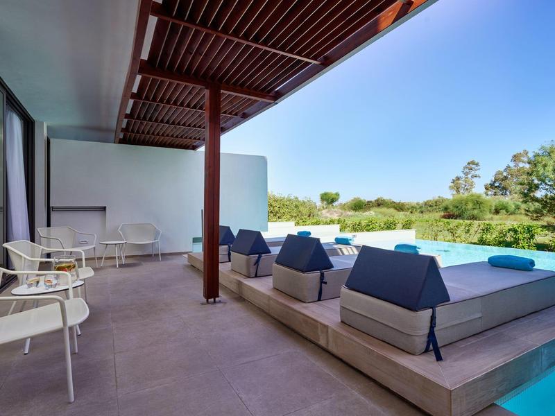 Terrazza moderna di un hotel con divani e piscina, circondata dal verde in una giornata di sole.