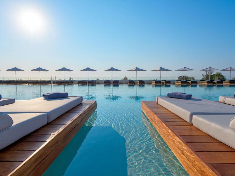 Piscina a sfioro con lettini e ombrelloni sotto un cielo limpido vicino al mare