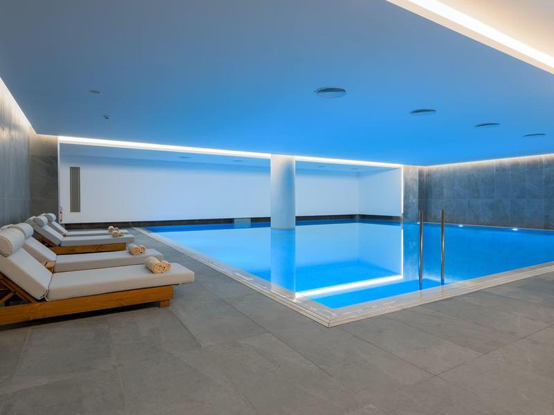 Piscina interna moderna con illuminazione elegante e comode sdraio.