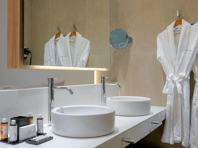 Bagno moderno con due lavabi, specchi e accappatoi bianchi appesi al muro.