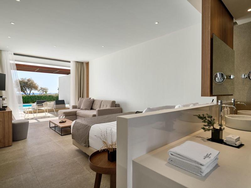 Camera d'hotel luminosa con letto, divano, TV e vista sulla piscina e terrazza.