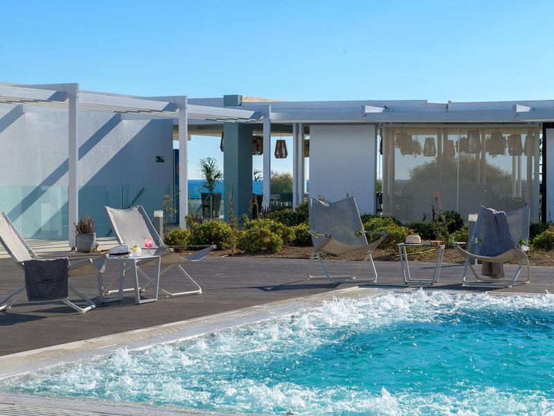 Piscina moderna dell'hotel con sedie a sdraio e ringhiera in vetro sotto il sole.