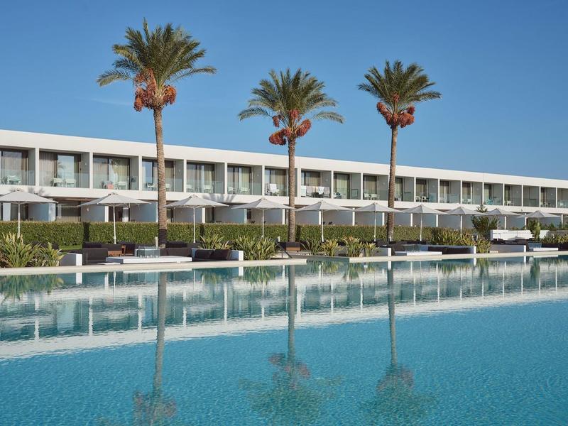 Hotel moderno con piscina e palme sotto un cielo azzurro limpido.
