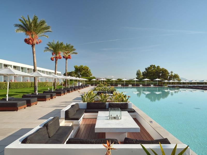 Area esterna moderna con salotti e piscina accanto a un hotel sotto la luce del sole.