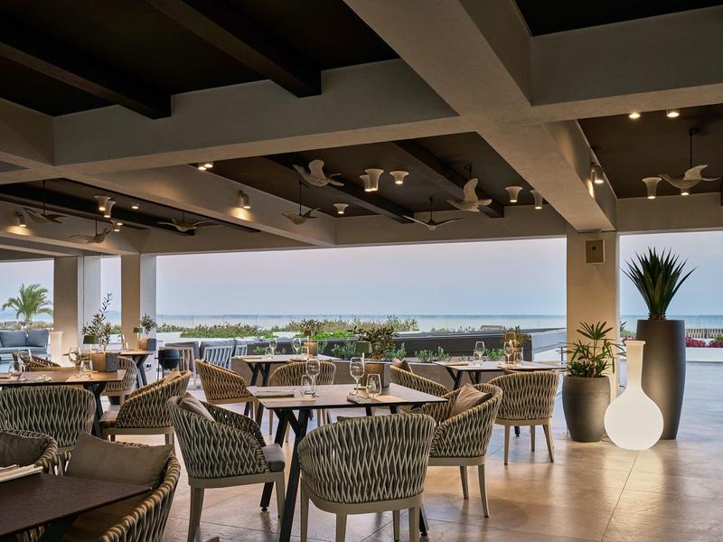 Area ristorante aperta con vista mare e sedie in vimini moderne.