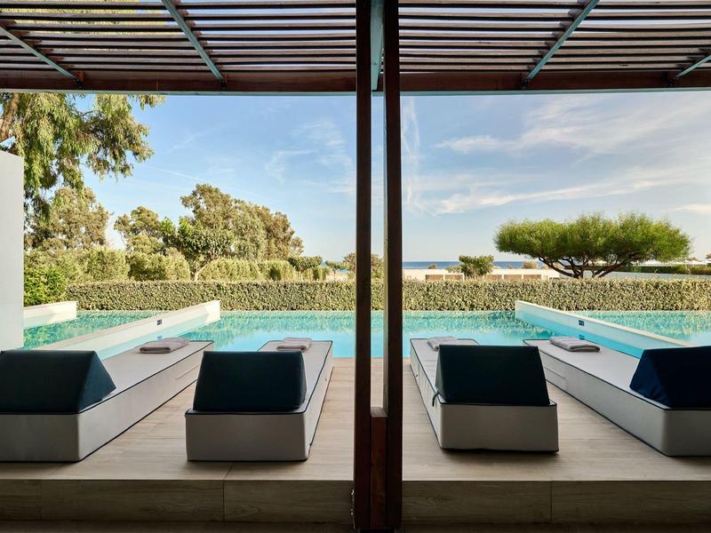 Vista da una terrazza coperta con lettini su due piscine e paesaggio verde.