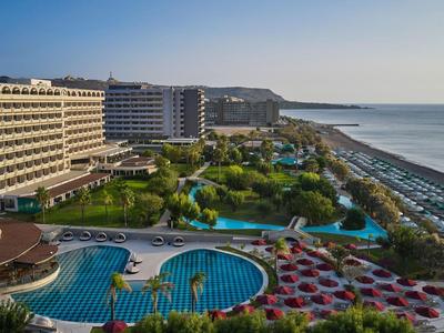 Großes Hotel mit mehreren Pools und Palmen am langen Sandstrand unter klarem Himmel.