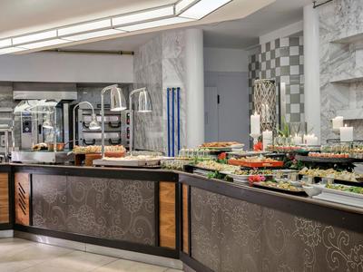 Modernes Buffet mit vielfältigen Speisen auf dunklem Tresen vor weiß-grauen Wänden und großem Fenster.