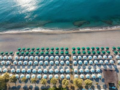 Luftaufnahme eines Strandes mit mehreren Reihen von Sonnenschirmen und Liegestühlen am klaren blauen Meer.