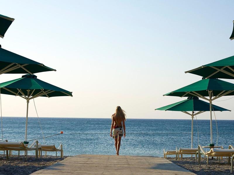 Vista di una piscina con lettini e ombrelloni di fronte al mare sotto un cielo sereno.