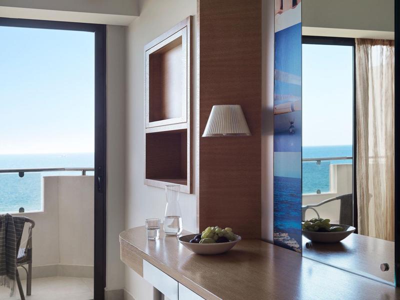 Camera d'hotel luminosa con balcone e vista mare, arredamento moderno e decorazioni.