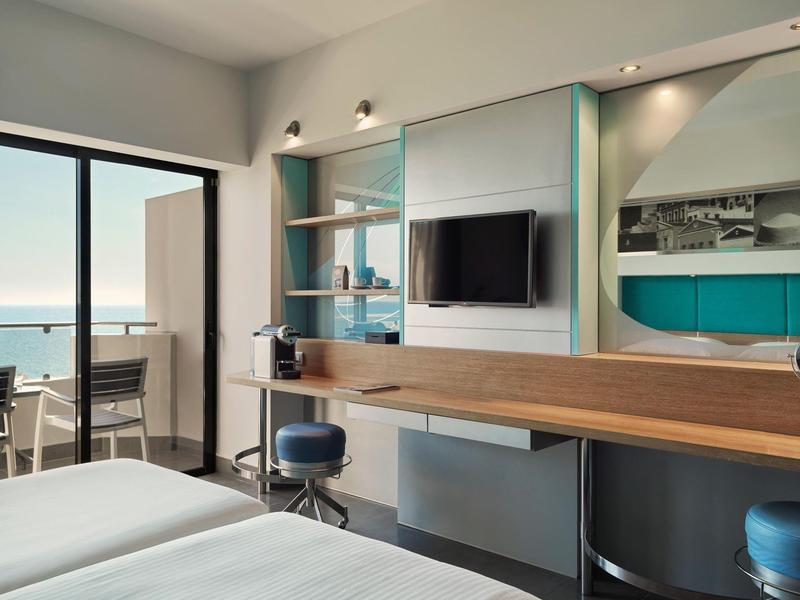 Camera d'hotel moderna con vista mare, balcone, scrivania e TV.