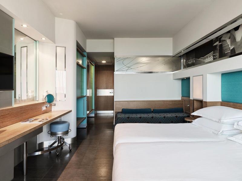 Camera d'hotel moderna con due letti, scrivania in legno e bagno sullo sfondo.