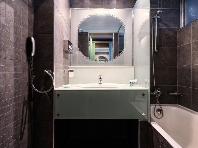 Bagno moderno con specchio rotondo, lavabo e vasca in piastrelle scure.