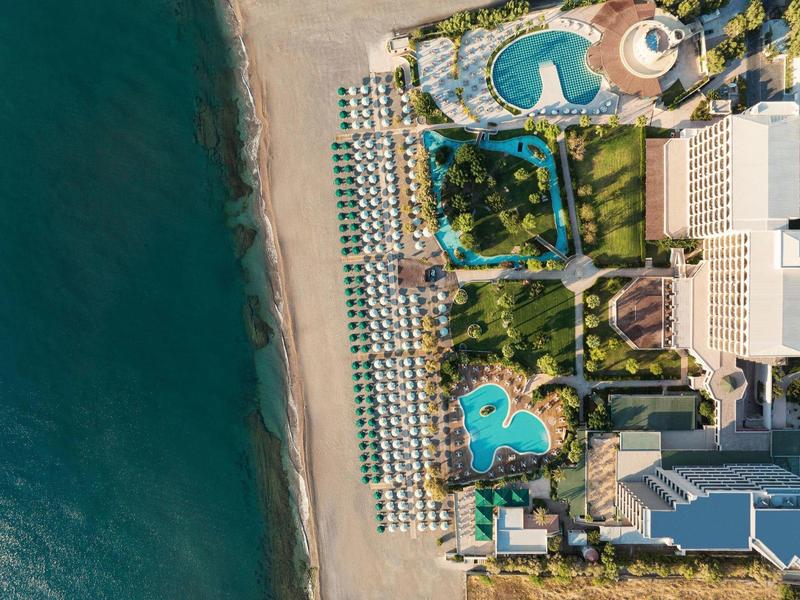 Veduta aerea di una zona resort con piscine e lettini vicino al mare.