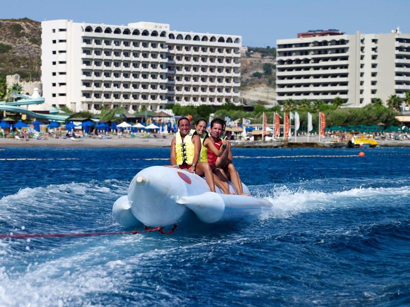 Vista sul mare con prato verde, alberi, piscina e spiaggia soleggiata.