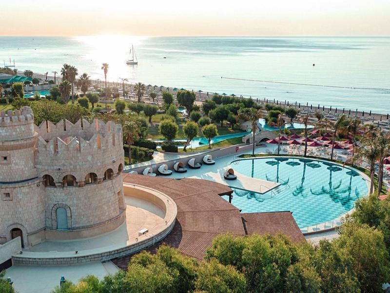 Torre storica vicino a una grande piscina con vista sul mare al tramonto.