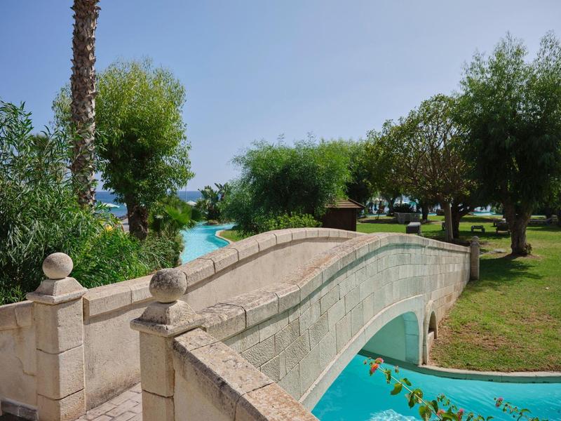 Ponte in pietra sopra una piscina in un giardino verde con alberi.