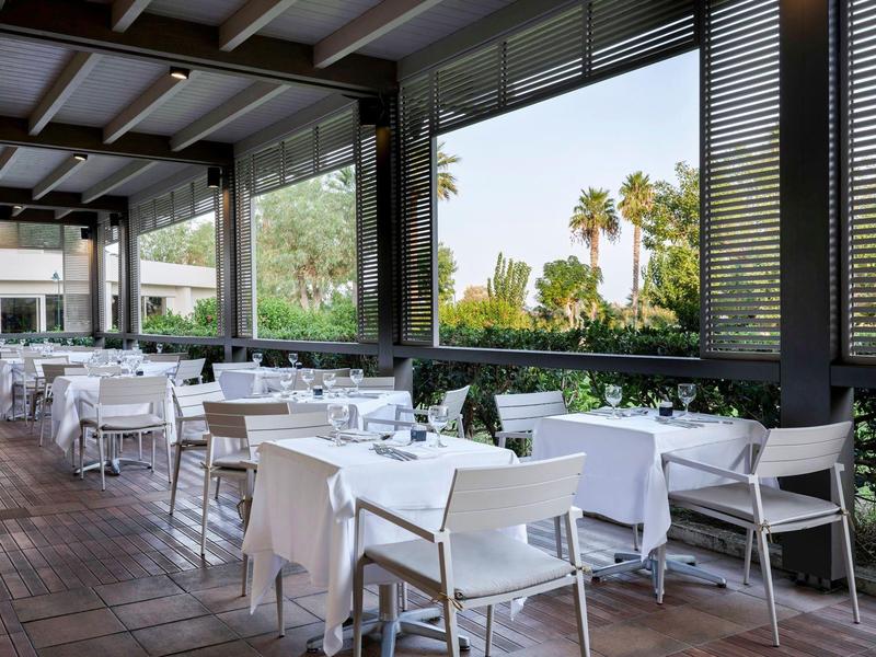 Terrazza di un ristorante d'hotel con tavoli bianchi e vista su palme.