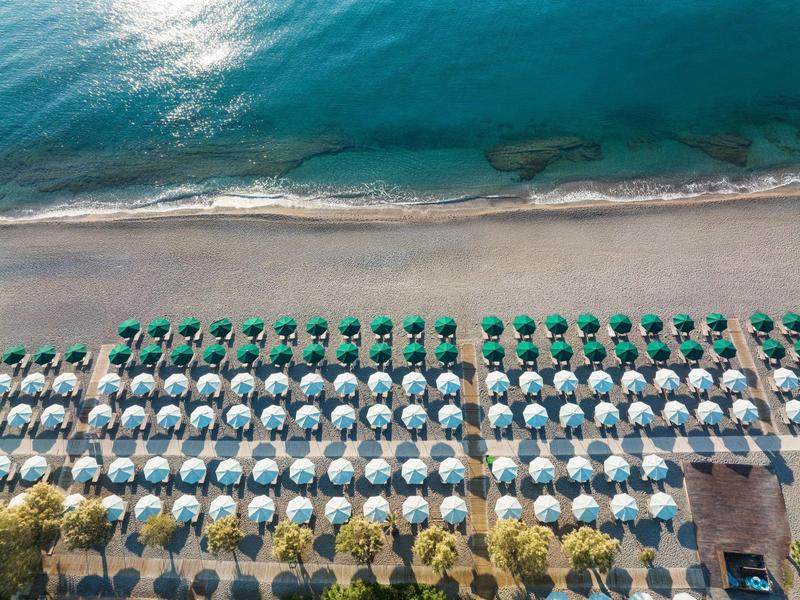 Vista aerea di una spiaggia con file di ombrelloni colorati e sabbia dorata.