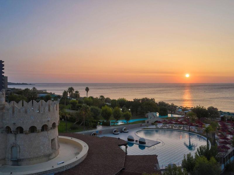 Tramonto su una località costiera con piscina, torre e vista sul mare.