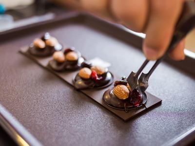 Mano che decora quattro piccoli dolci al cioccolato disposti su una base rettangolare di cioccolato