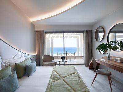 Luminoso camera d'hotel con letto, due poltrone e balcone con vista oceano