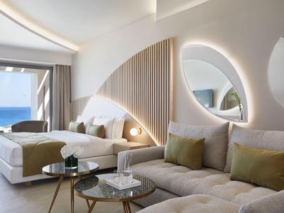 Camera d'hotel moderna con vista mare, letto matrimoniale, divano e specchi rotondi sulla parete.