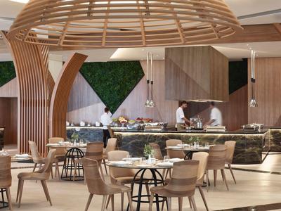 Ristorante moderno con elementi in legno, aree salotto varie e stazione buffet sullo sfondo.