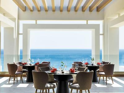 Terrazza del ristorante con vista sul mare, tavoli apparecchiati e sedie moderne sotto una pergola.