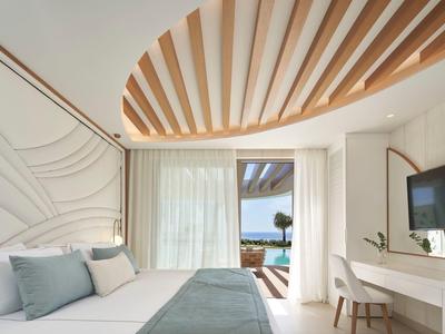 Camera d'hotel luminosa con arredamento moderno, vista mare e scrivania con TV a parete.