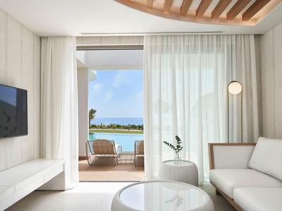 Camera d'hotel luminosa con mobili bianchi che si apre su balcone con vista mare.