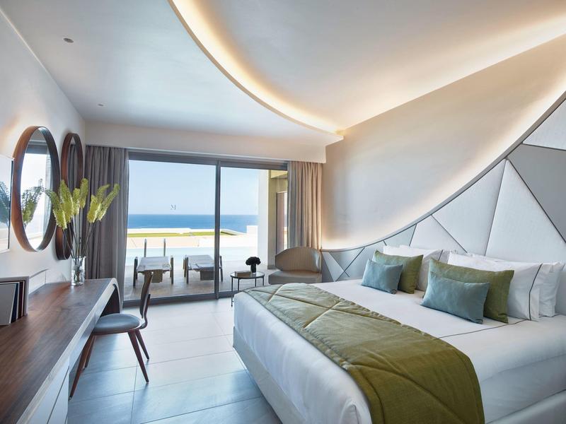 Camera d'hotel moderna con vista mare, letto grande, balcone e illuminazione elegante.