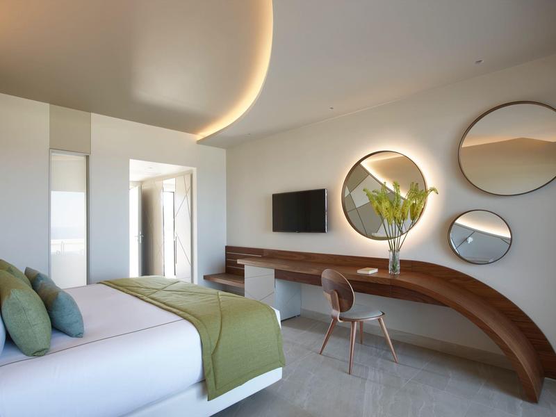 Camera d'hotel moderna con scrivania curva, specchi rotondi e letto king size con accenti verdi.