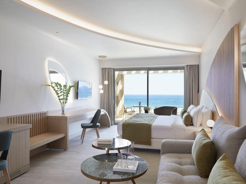 Camera d'hotel moderna con vista mare, letto matrimoniale, divano, scrivania e balcone.