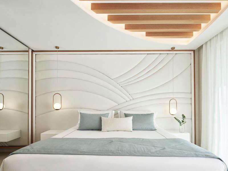 Camera da letto moderna e luminosa con parete strutturata, grande letto e luce naturale soffusa.