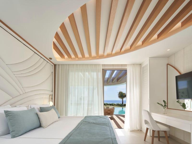 Camera d'hotel luminosa con arredamento moderno, vista mare e scrivania con TV a parete.