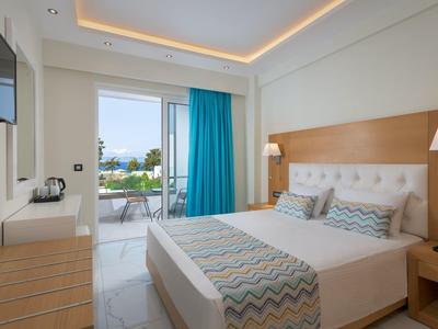 Habitación de hotel luminosa con cama doble, cortina turquesa y vista a terraza con piscina.